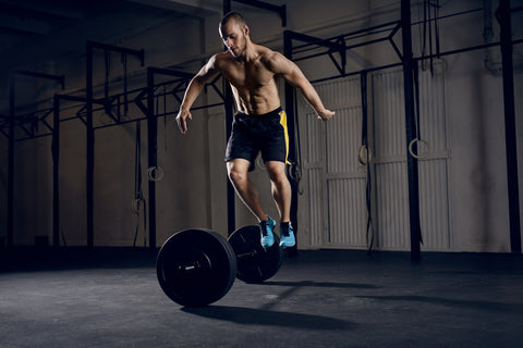 Man jumping over barbells during burpees exercise