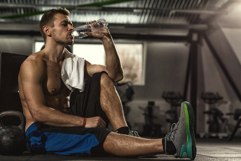  Shirtless sportsman resting after training at the gym sitting on the floor drinking water 