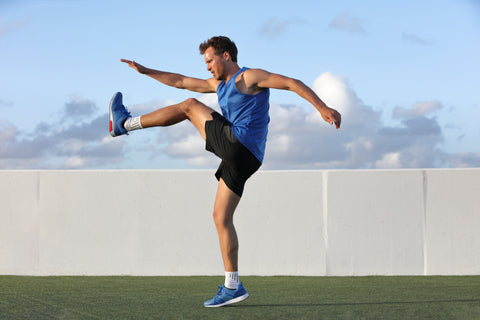 Runner man getting ready to run doing warm-up dynamic leg stretch exercises