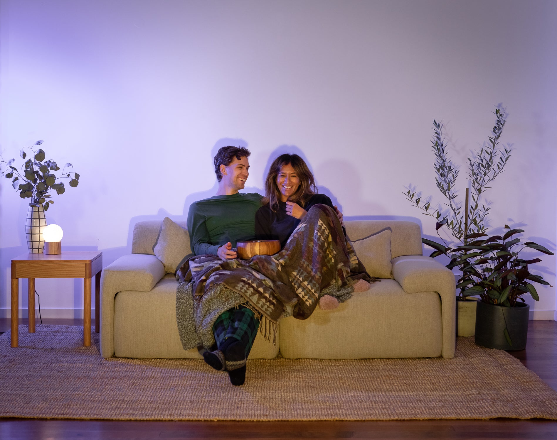 dark living room, a smiling couple sitting on the Eva Everyday Sofa, watching a TV (offscreen)