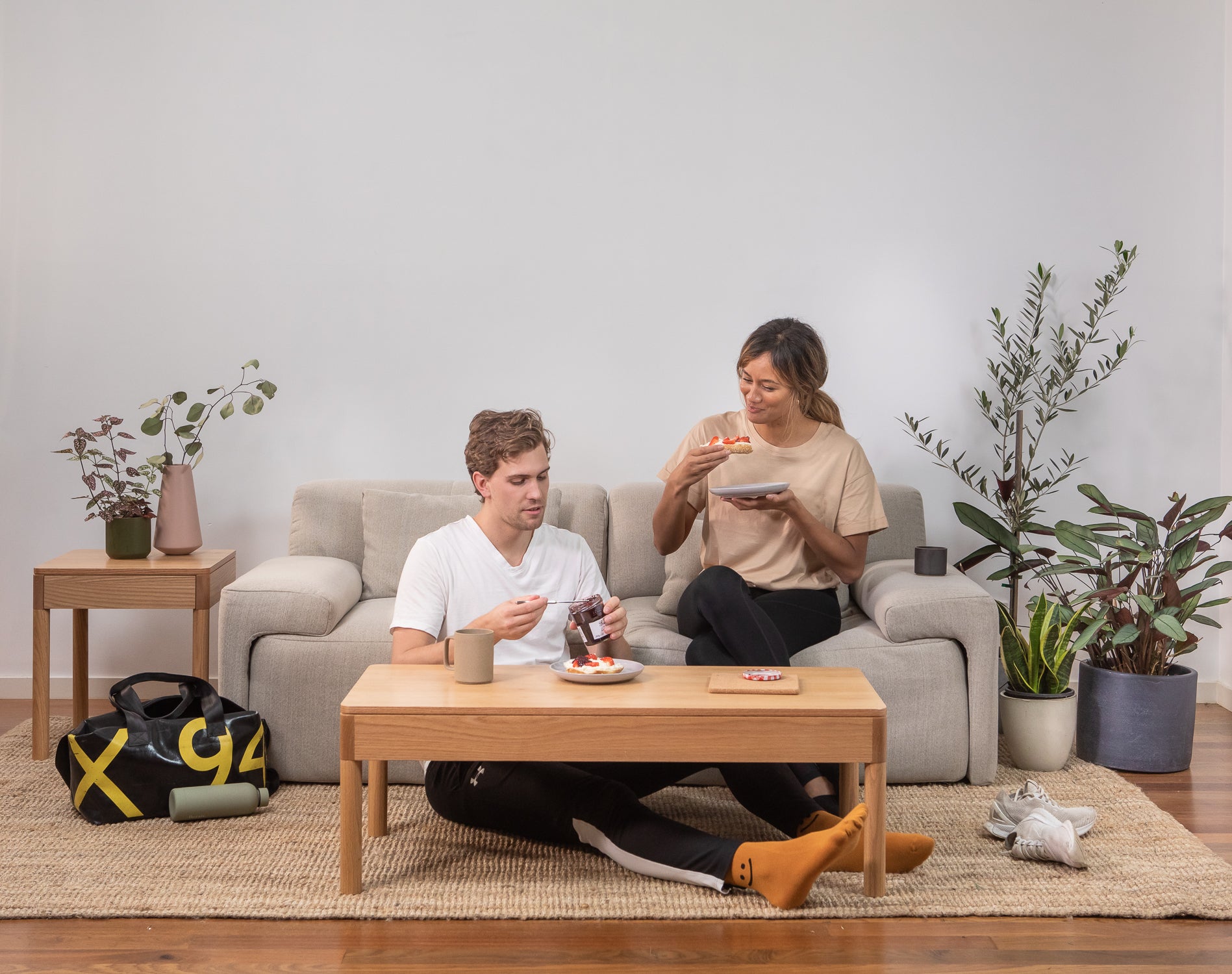 A couple sit on the Eva Everyday sofa in a living room, eating bagels