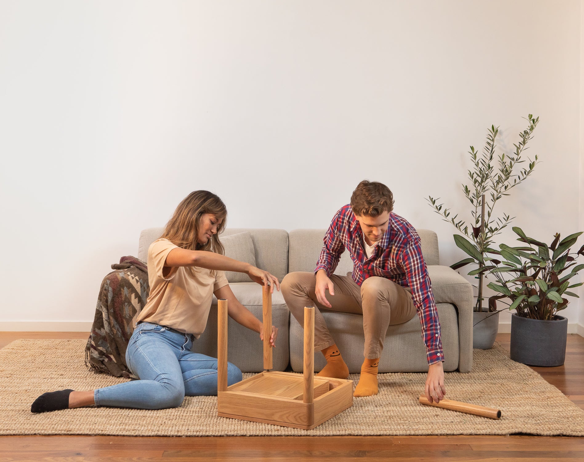 A couple, man and woman, assemble the Hideaway side table in their living room with the Everyday Sofa behind them.