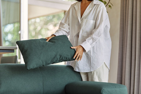 Everyday sofa in moss green, woman holds a cushion and is placing it on the sofa