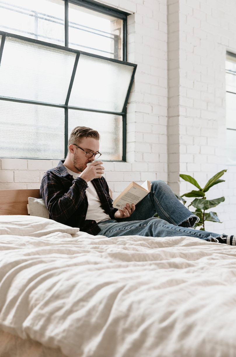 Guy with glasses drinks coffee on oat coloured hemp linen sheets