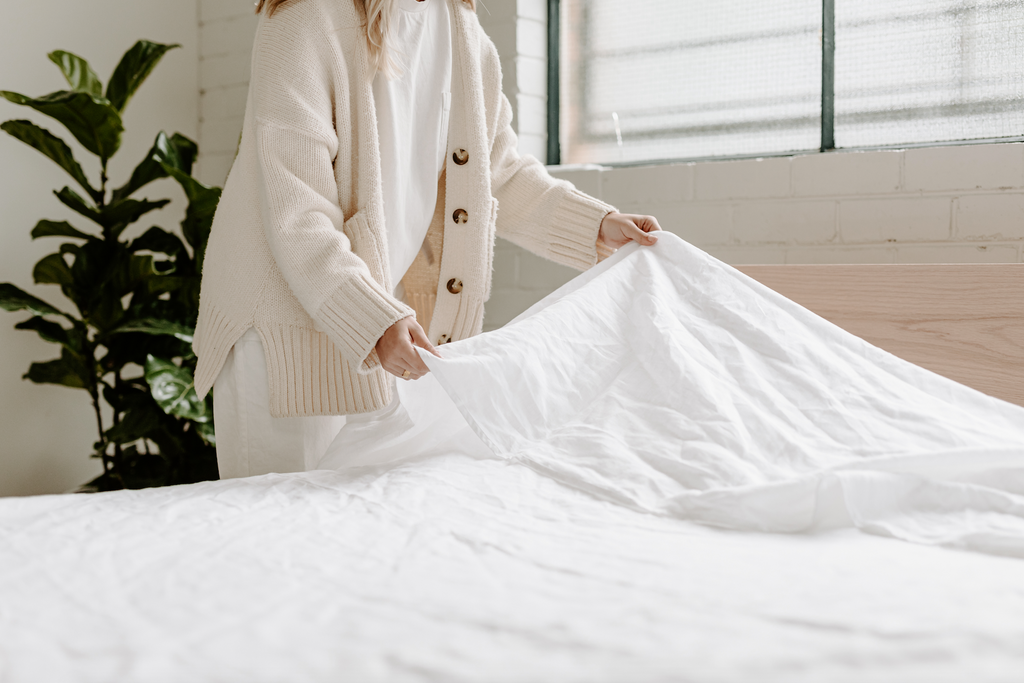 Girl making bed with white sheets made from hemp linen 