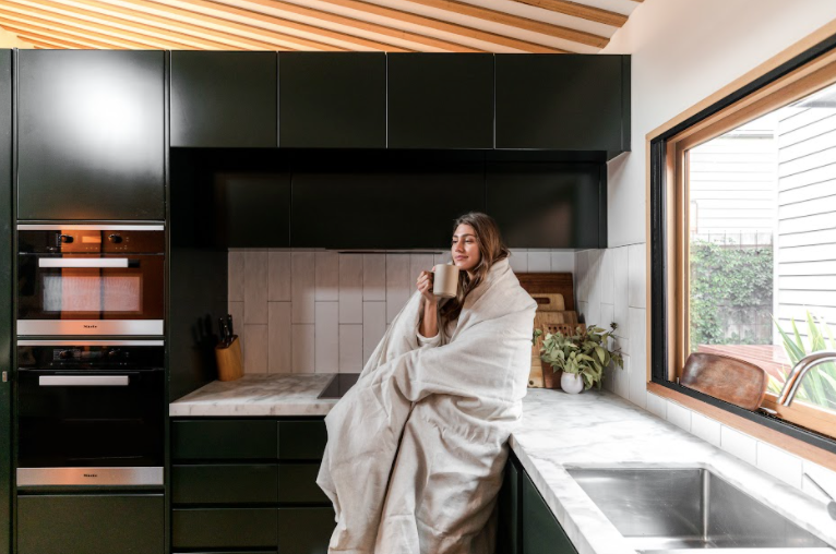 Woman drinking coffee in kitchen rugged up in eva hemp linen duvet