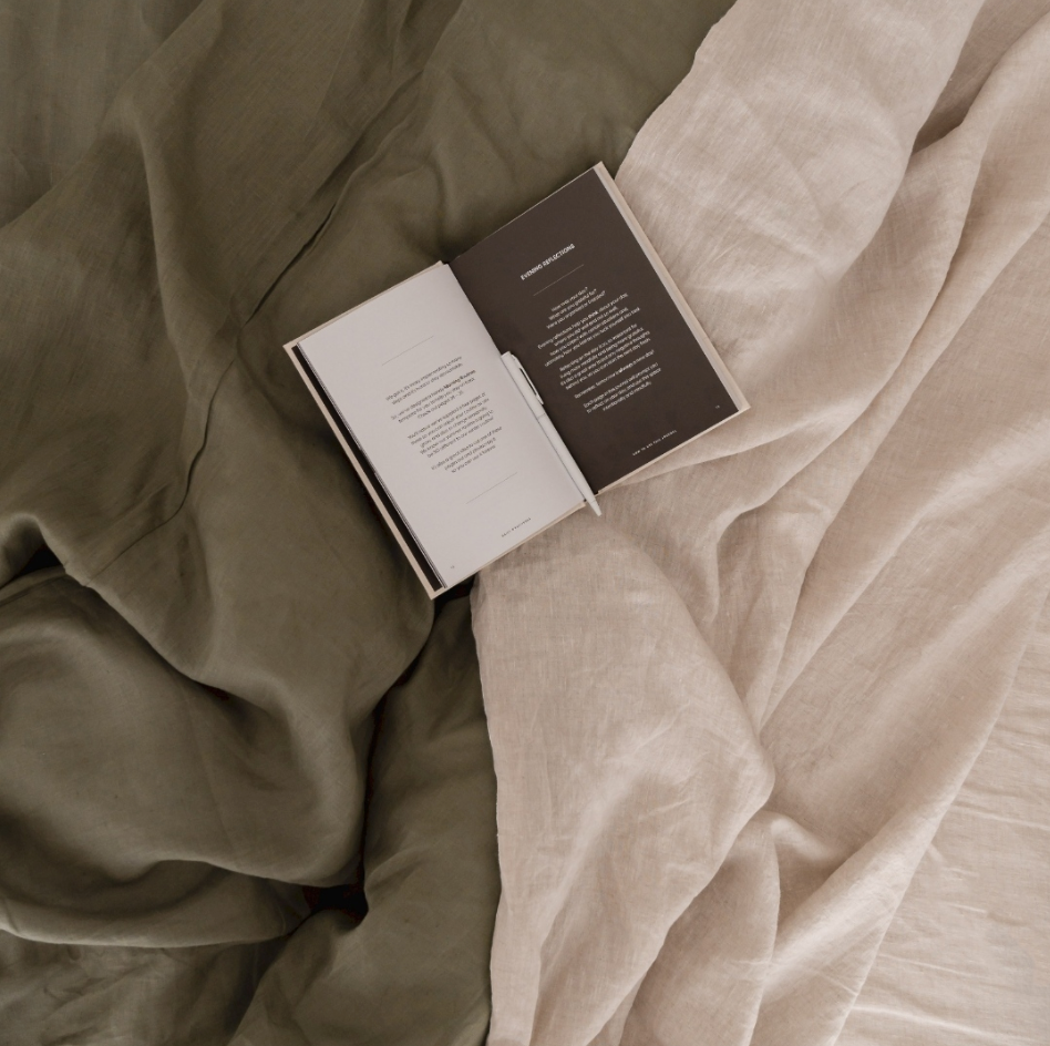 eva hemp linen sheets in oat and olive spread over a bed, with a book lying in the centre