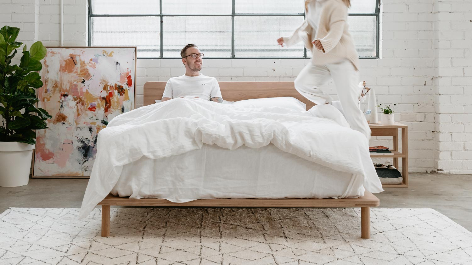 Young woman jumping on to mattress next to partner