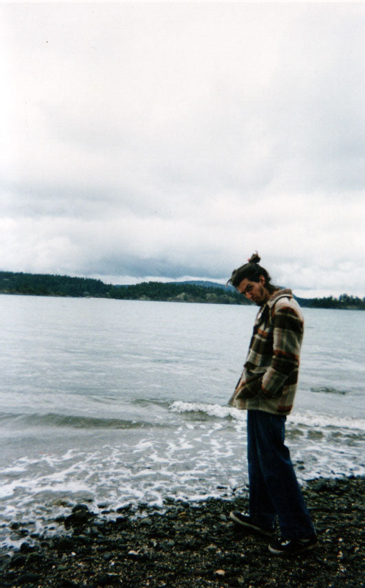 man in multicoloured coat standing on a rocky beach on a cloudy day looking left