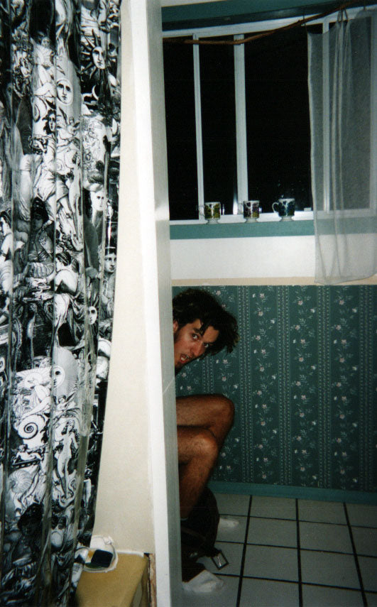 man's legs sticking from around a corner below his head which appears to be rather unimpressed by being photographed on the toilet