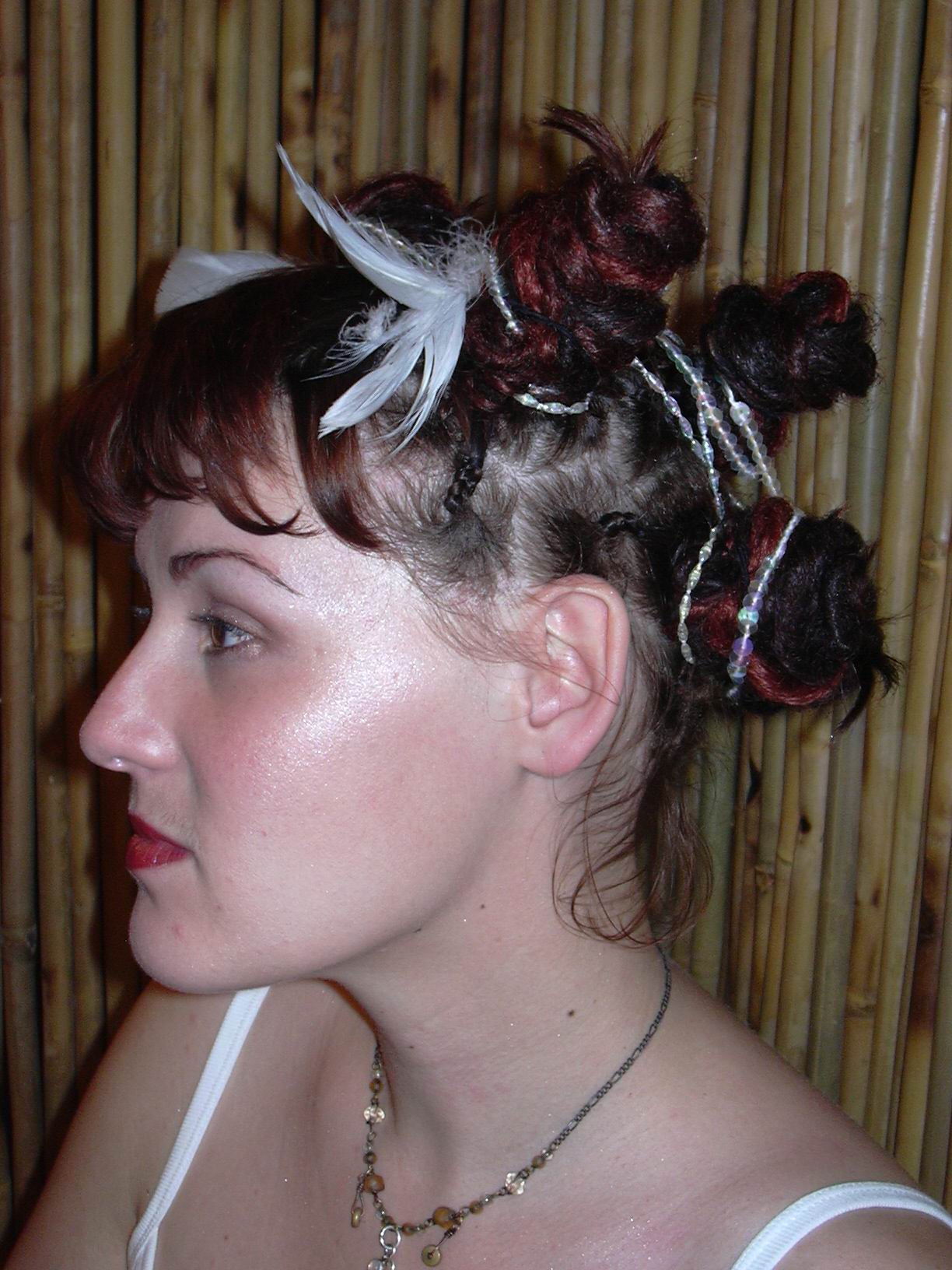 side view of woman in white camisole with neutral expression showing tightly wrapped bunches of dreadlocks