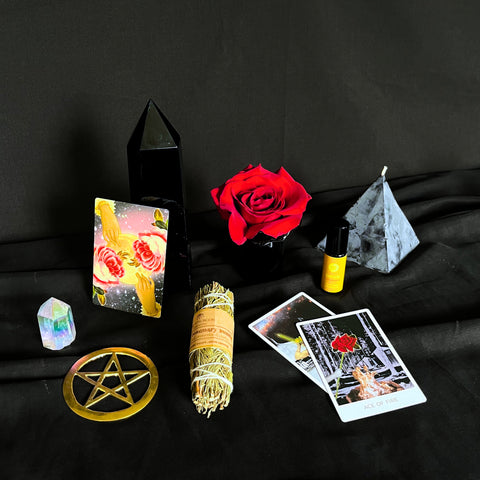 Altar set up in black, red, and yellow with tarot cards, herb bundle, gold pentacle, a rose, a candle, and body oil