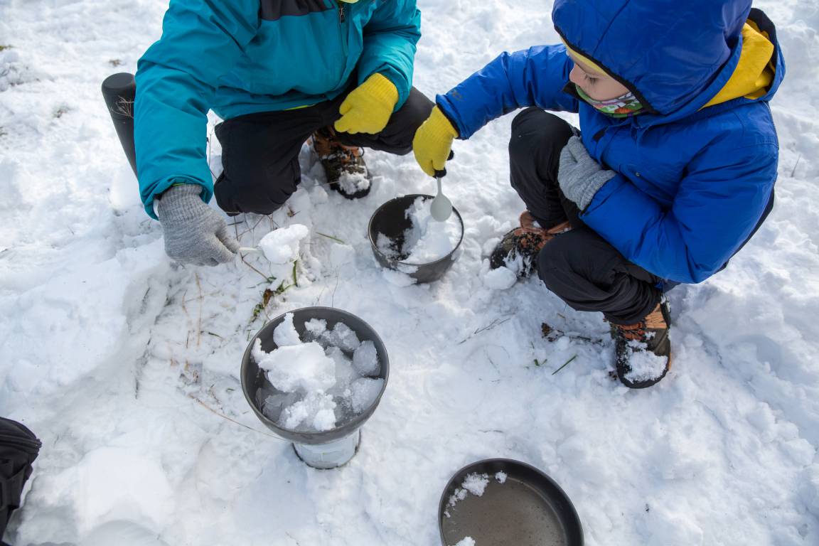 Kids adding snow to pots to boil water