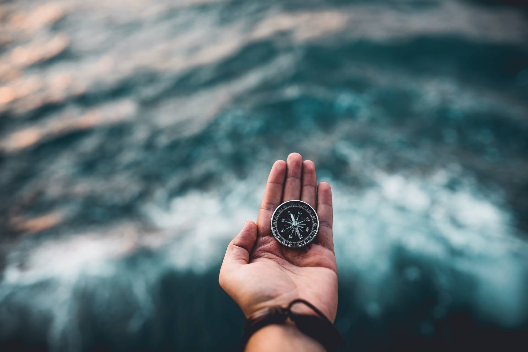 Man holding a compass in front of an ocean tide