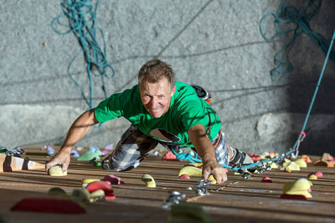 Mature adult climbing an indoor climbing wall in a green shirt