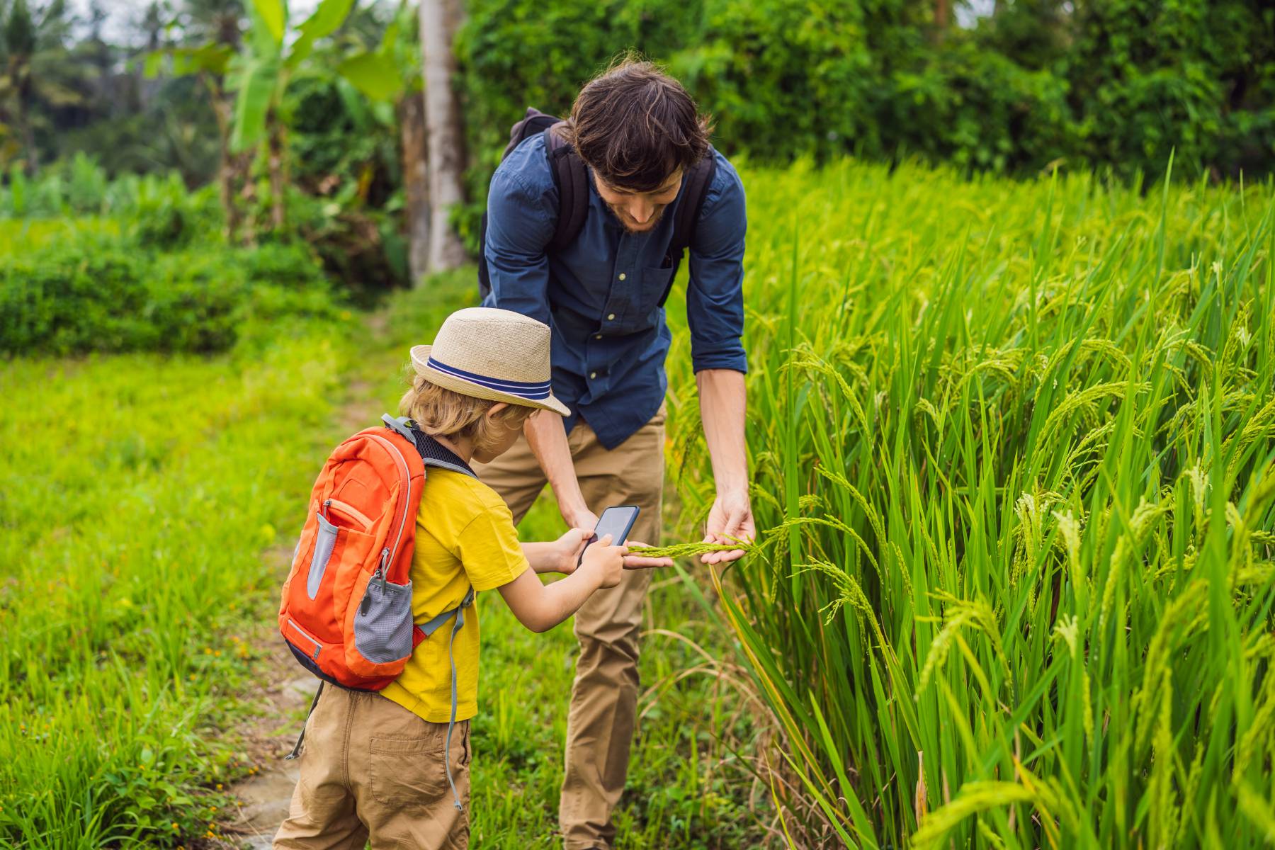 Man in navy blue shirt showing child in yellow shirt with a sun hat how to forage