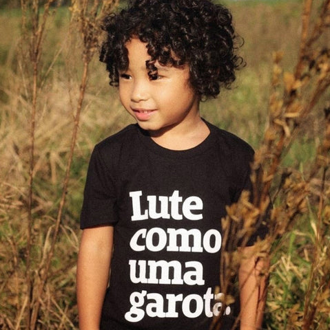 foto de un chico oriental, de pelo castaño rizado, vestido con un pecho negro con la frase pelea como una chica de blanco