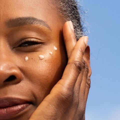 An elegant woman with gray hair applying eye cream under her eyes for skincare.