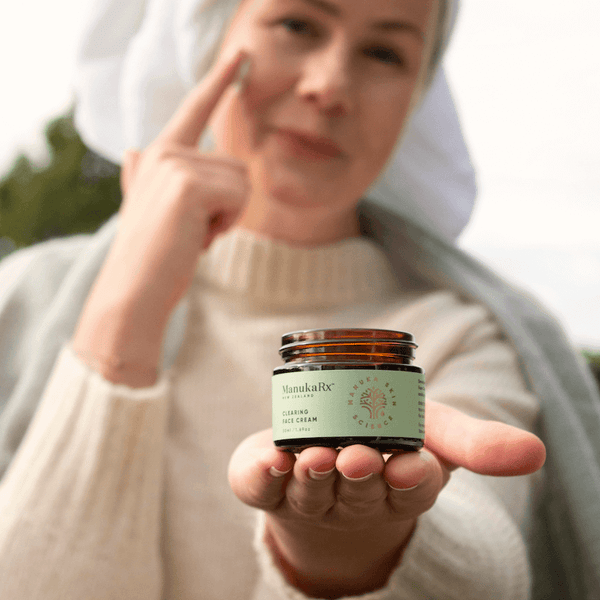 Banish Blemishes Naturally with Mānuka Oil image showing a woman with beautiful skin in a towel moisturising with ManukaRx Clearing Face Cream.