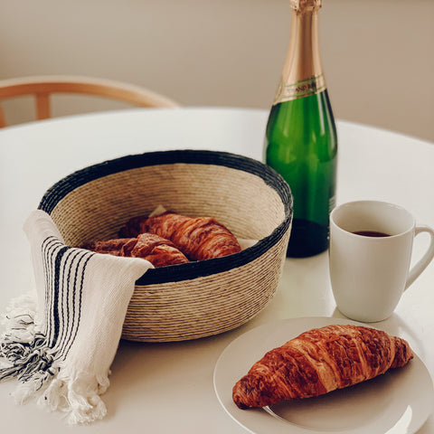 The handcrafted Torrey circle basket holding croissants, decorated nicely on a breakfast table.