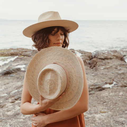 Leah collection of palm straw hats - the Moonlight hat on a model while holding the Vagabond Gambler style.