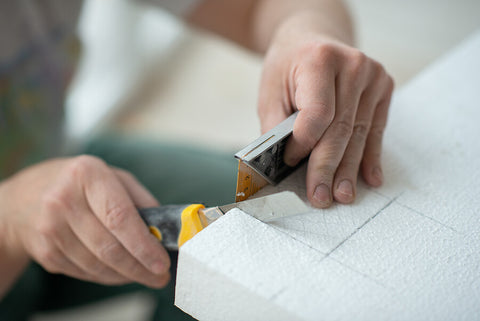 Two hands measuring and cutting a piece of polystyrene.