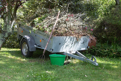 A trailer full of garden waste with a pitchfork and a green bucket, located in a garden