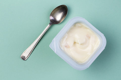 An aerial view of a yoghurt pot and a metal spoon on a light green background.
