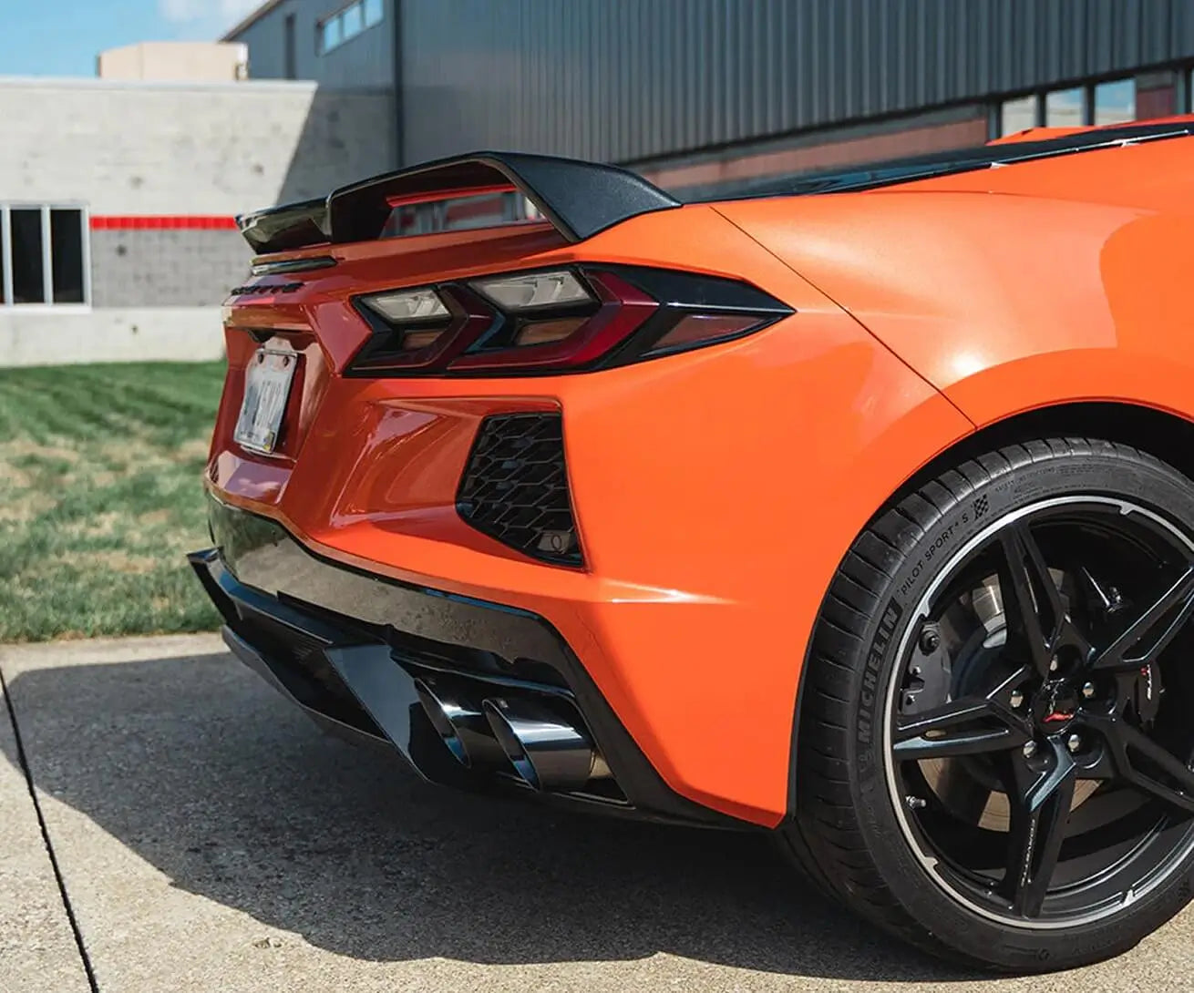 Rear-side view of an orange Chevrolet Corvette C8 parked near a modern building.