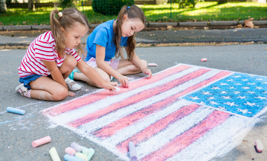 Two young girls painting an American flag on the driveway with chalk