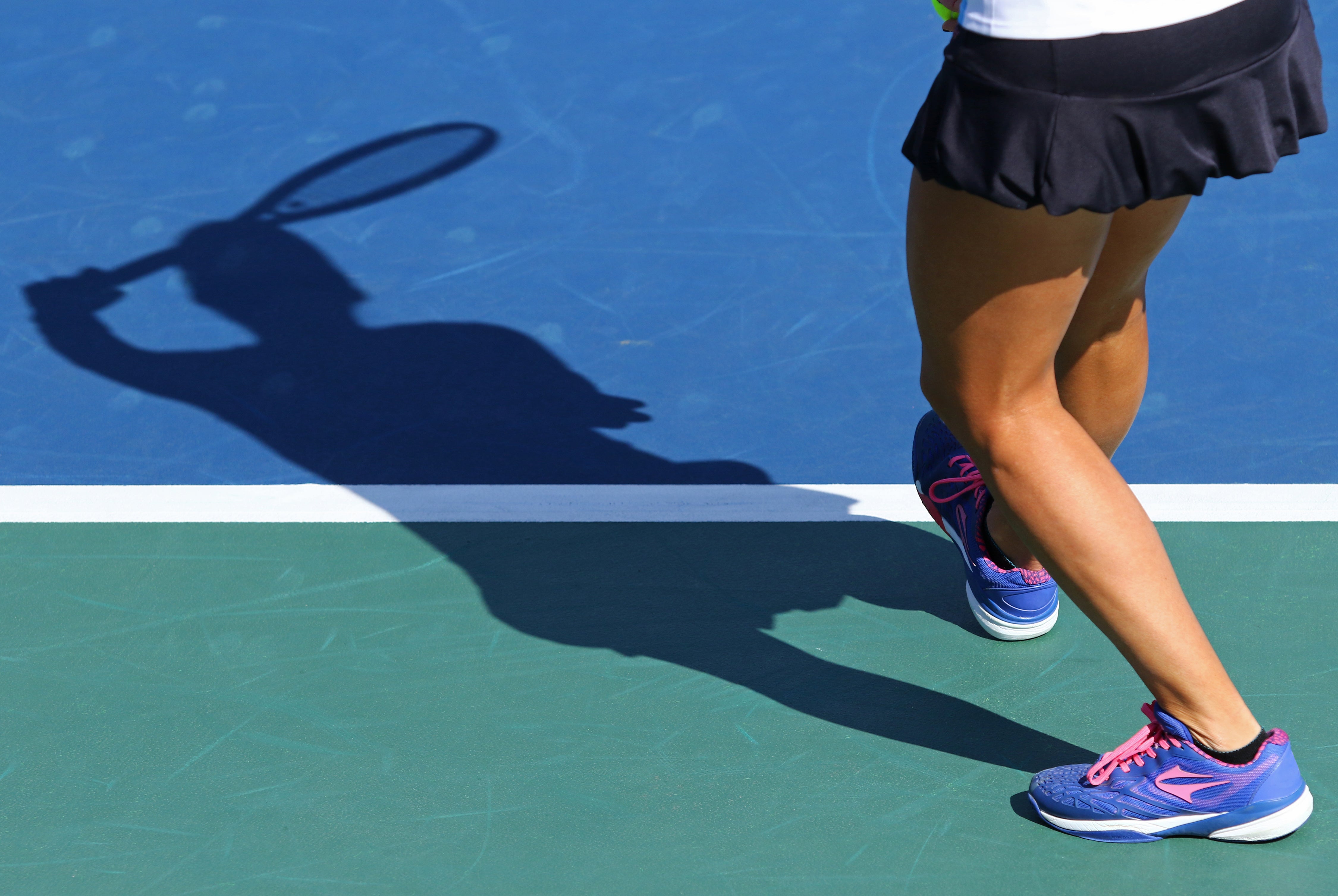 Woman's legs and sneakers close to the baseline on tennis court