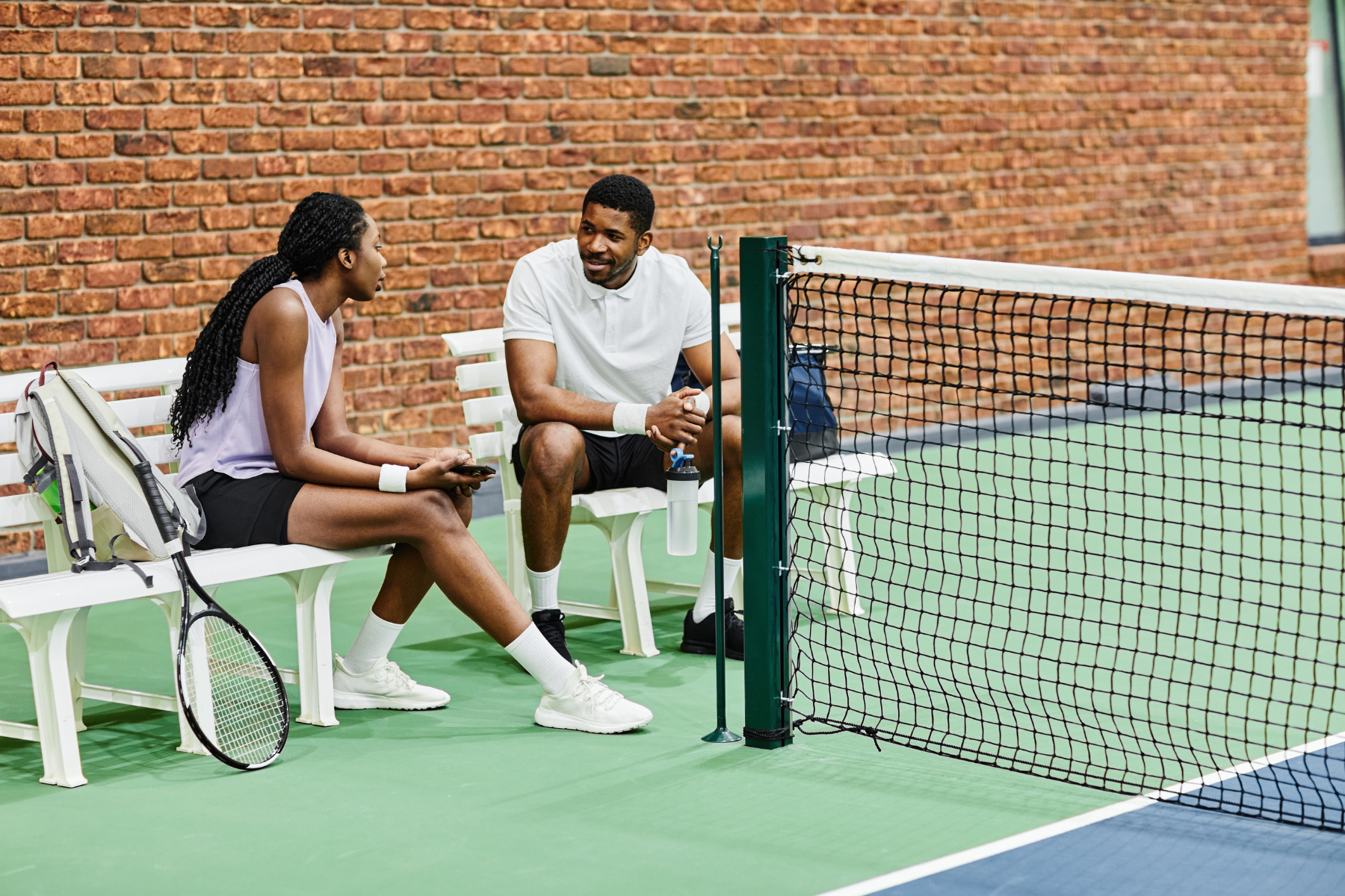 man and woman sitting on bench next to tennis court talking