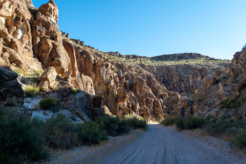 A dirt road alongside sandy geologic formations and blue sky.