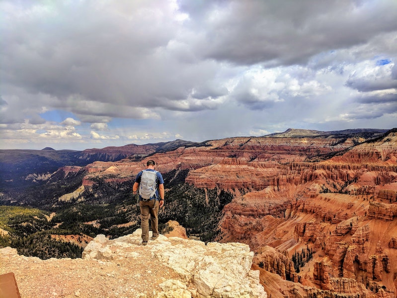 Person stands on rocky overlook of orange canyon.