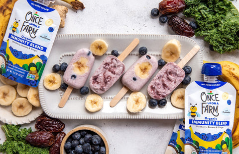 blueberry yogurt pops on a tray, next to fresh fruit and veggies and Once Upon a Farm Blueberry, Banana & Ginger Immunity Blend pouches