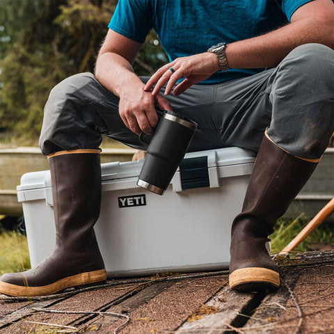 man sitting on YETI cooler, holding a YETI mug