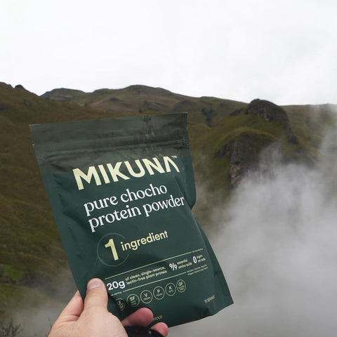 Hand holding a bag of MIKUNA pure chocho protein powder atop a mountain