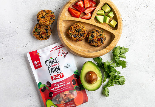 black bean and red pepper veggie burgers on a plate with avocado and strawberries, next to the Once Upon a Farm Black Bean & Red Pepper Meal package