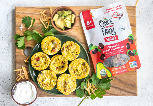 southwest egg bites on a cutting board with sour cream, avocado, cilantro, and the Once Upon a Farm Black Bean & Red Pepper Meal