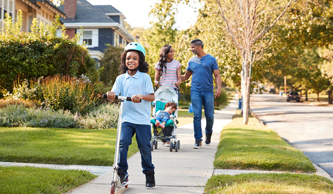 child riding a scooter, while mom and dad walk behind with a sleeping child in a stroller