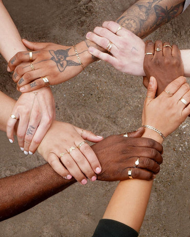 hands touching each other in a circle, all wearing rings by Automic Gold