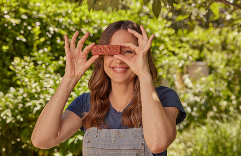 Once Upon a Farm Co-founder Jennifer Garner, holding an unwrapped Strawberry Refrigerated Oat Bar over her eyes