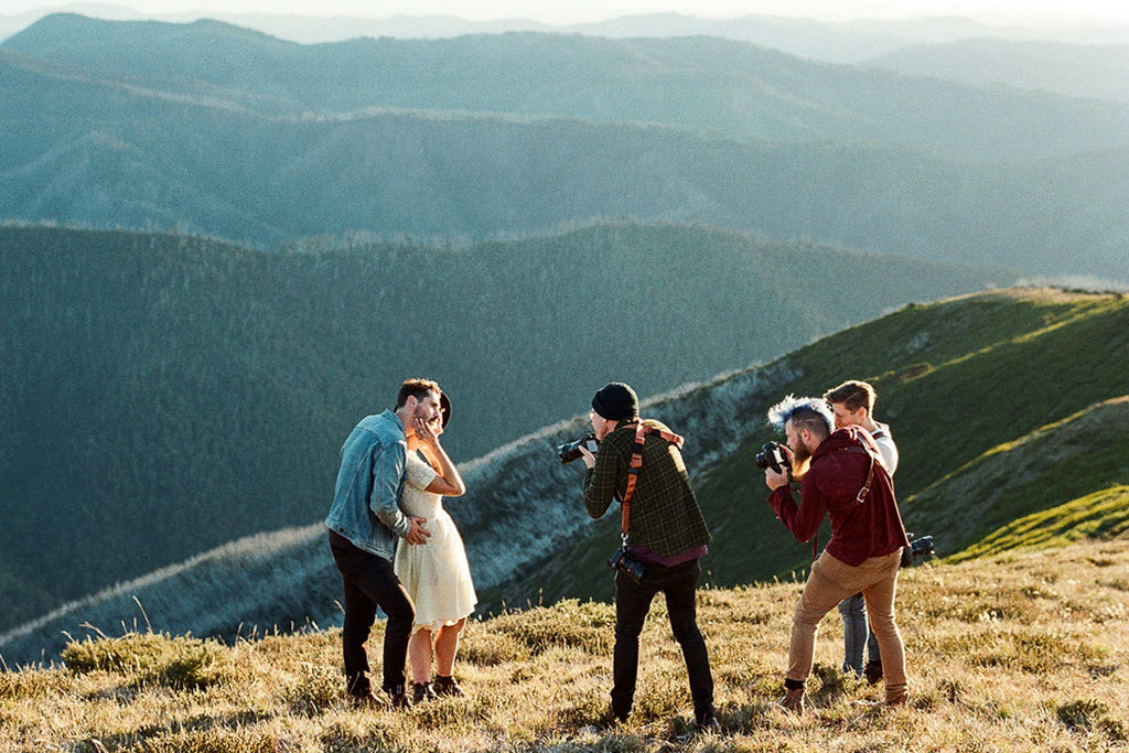 Male and female couple pose in front of a photography group on top of a mountain