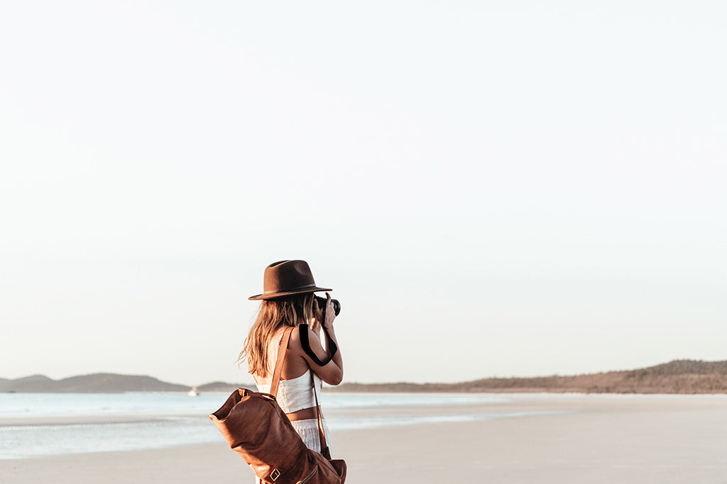 Lauren wearing William Brown hat taking a photo of a subject on the shoreline