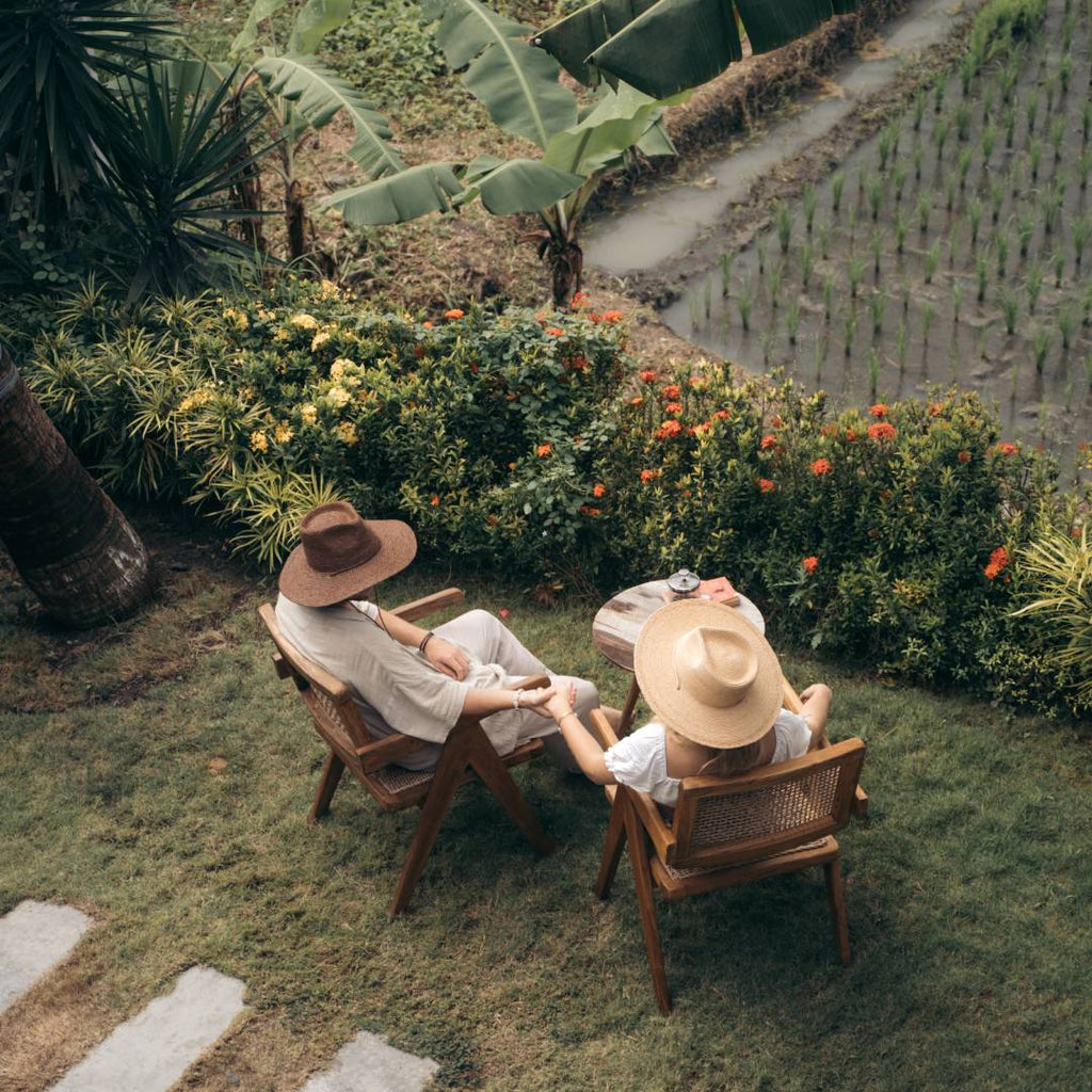 Man with short hair and woman with long blonde hair sitting at villa with straw hats on