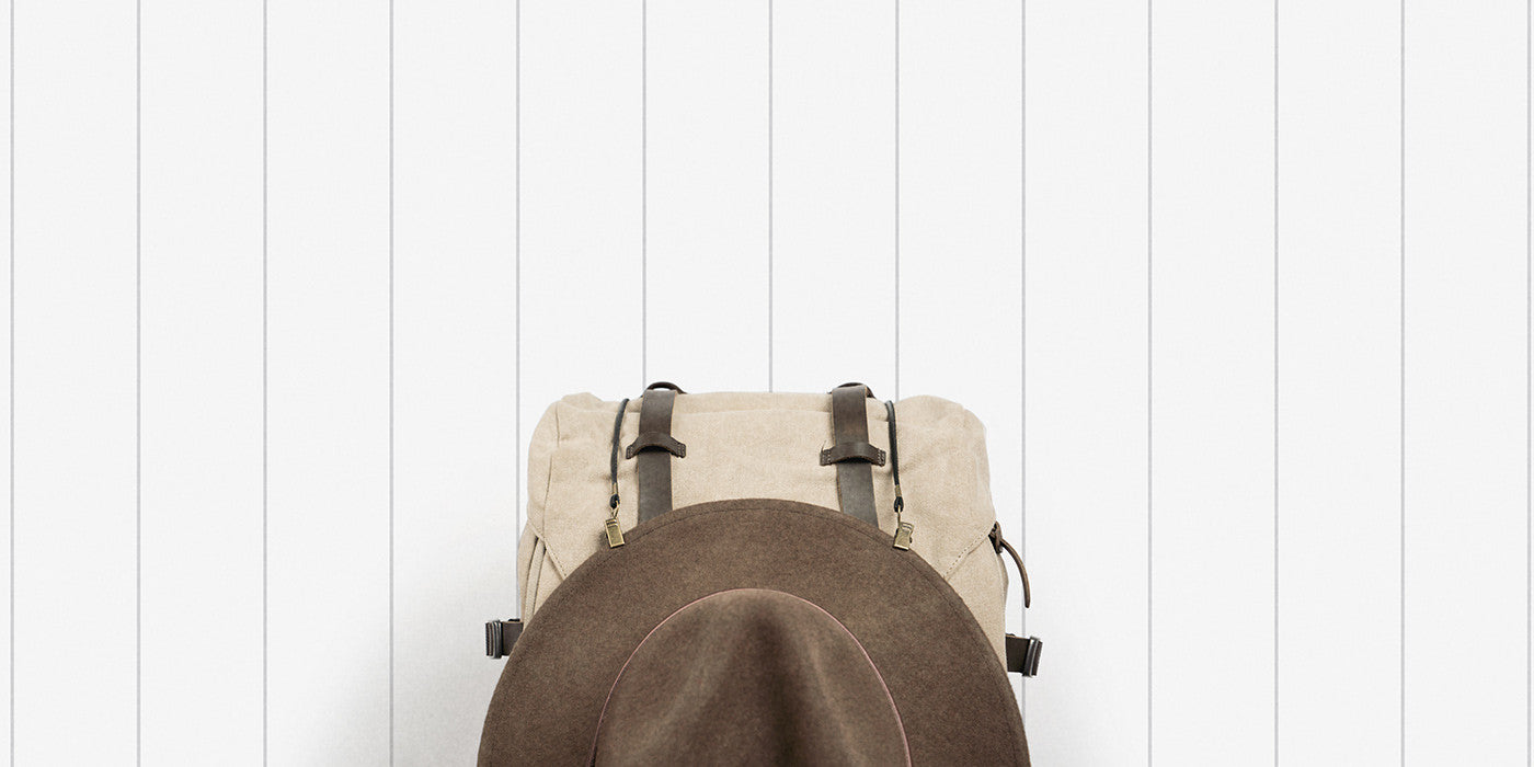 alt='back pack against white wall with Will & Bear hat attached on front'
