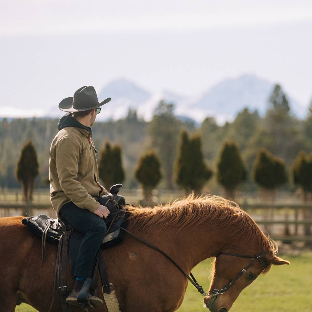 Man wearing Buck smoke black cowboy hat while riding a horse