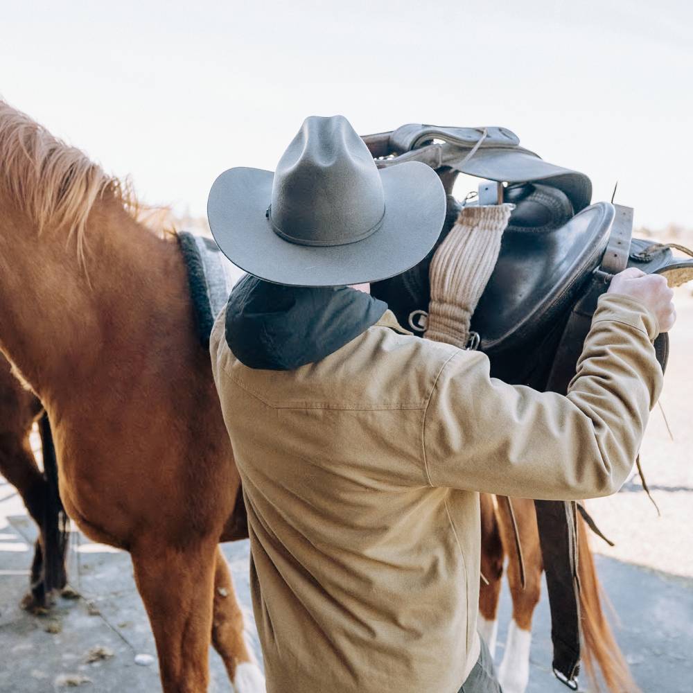 Man saddling up a horse wearing Buck smoke black cowboy hat