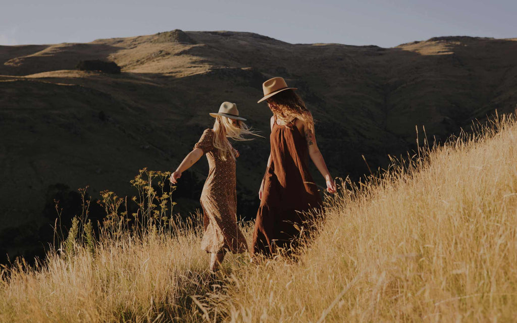 Women wearing wide-brim floppy hats and dress on a hill