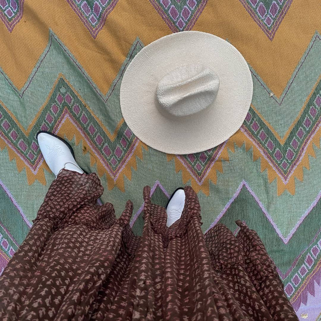 A photo of a woman's boots next to her cowboy hat sitting on top of a picnic blanket